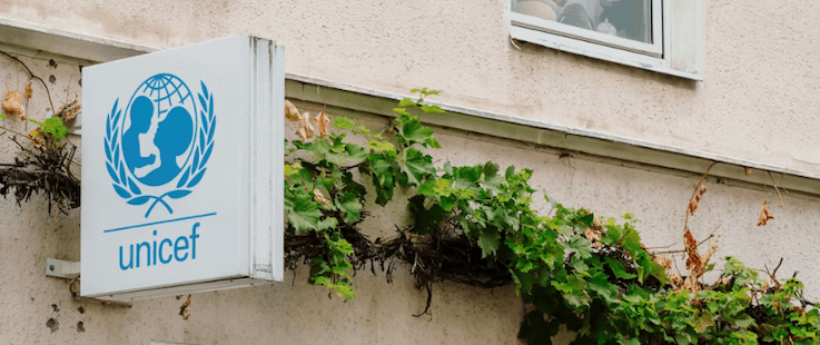 UNICEF appel aux dons affiche blanc bleu sur mur beige avec végétation