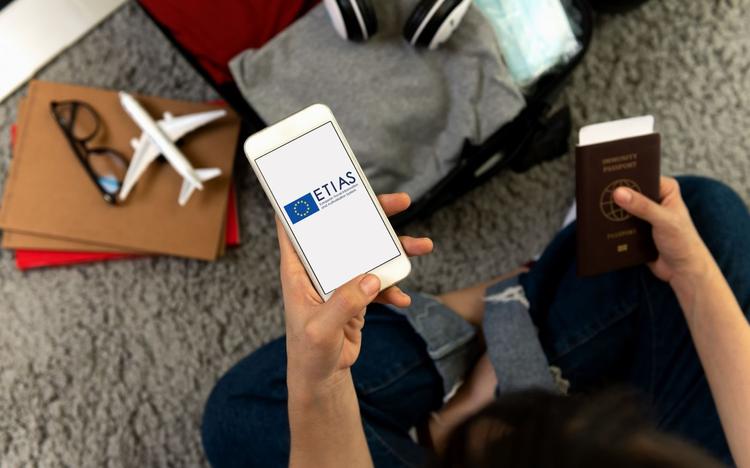 Une personne tient dans sa main gauche un téléphone affichant "etias" et dans l'autre un passeport.