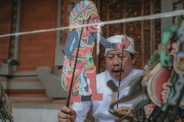 un homme balinais habillé en blanc qui tient une marionette traditionnelle