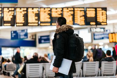 une personne attend à l'aéroport devant le tableau d'affichage avec son bagage