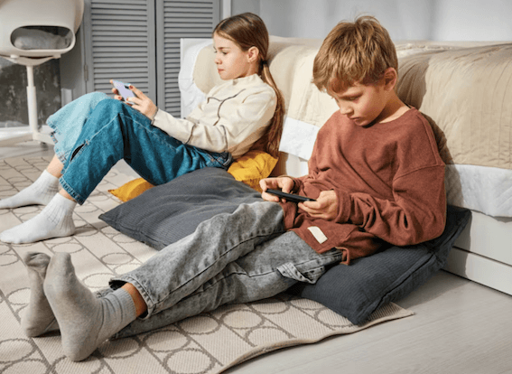 2 enfants une fille et un garçon assis sur un canapé beige qui regarde les écrans et réseaux sociaux